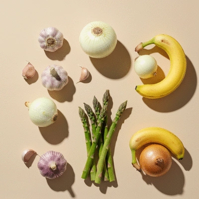 A colorful flat lay of prebiotic-rich foods like garlic, onions, bananas, and asparagus on a light background. Bright, clean, and fresh.